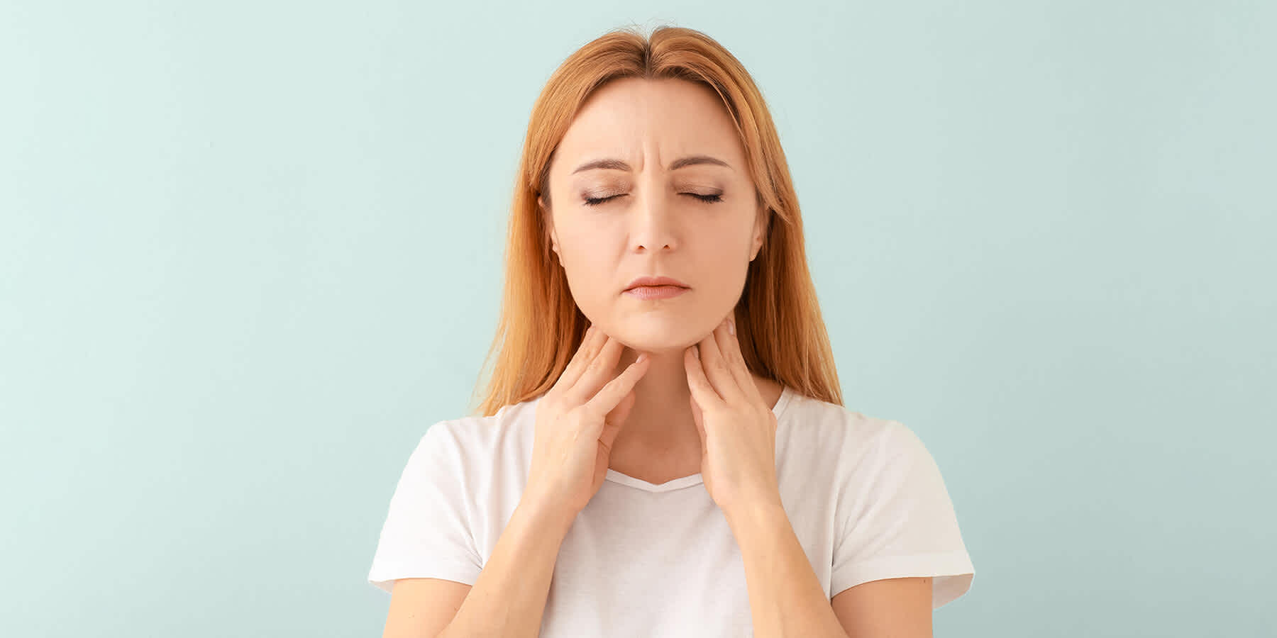 Woman with genetic thyroid problem feeling thyroid gland with her hands on her neck