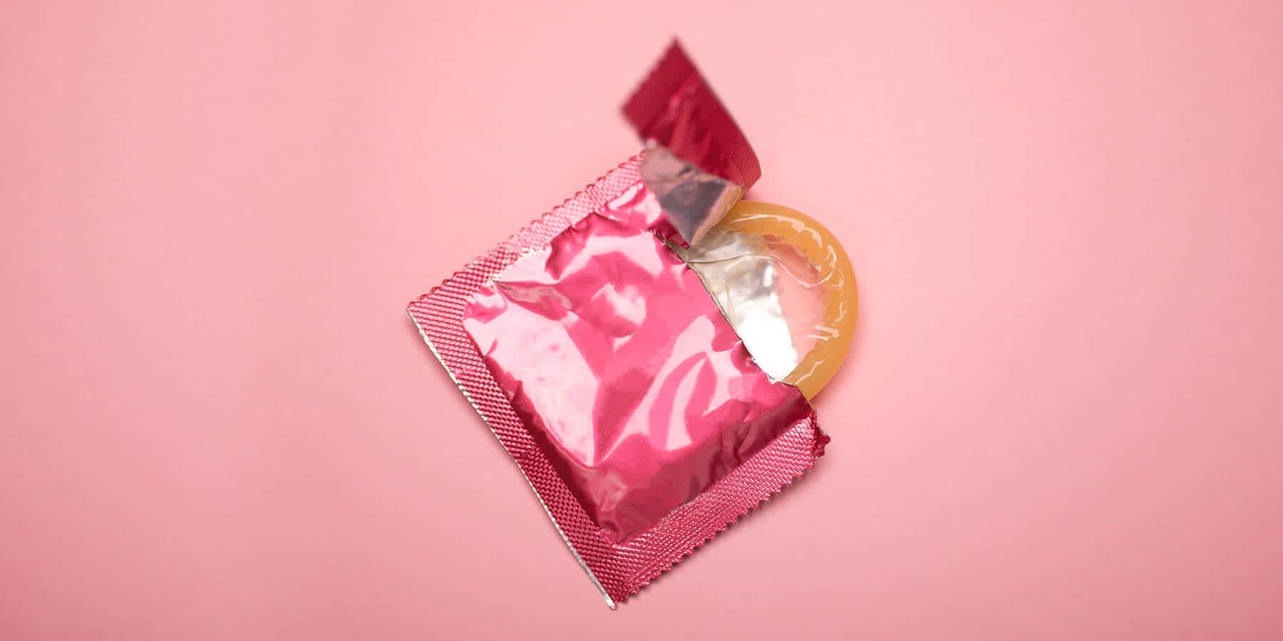 Opened condom packet against a light pink background