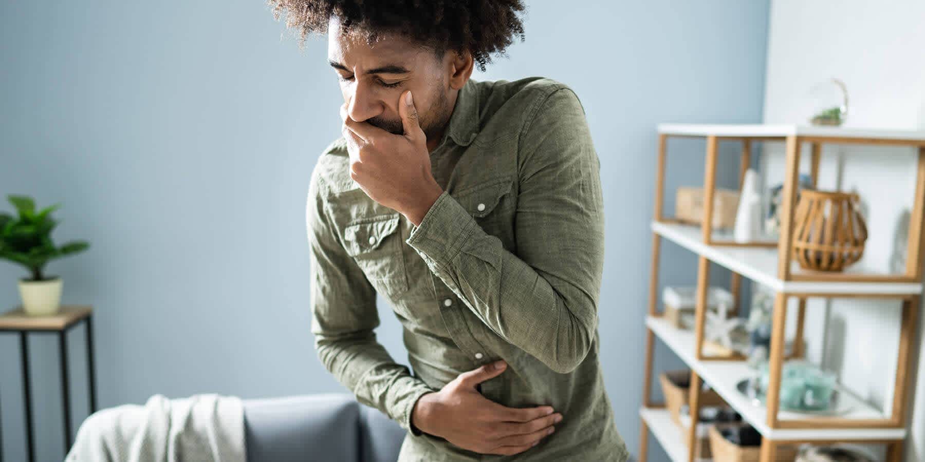 Man needing flu treatment with one hand over his stomach and other hand over his mouth