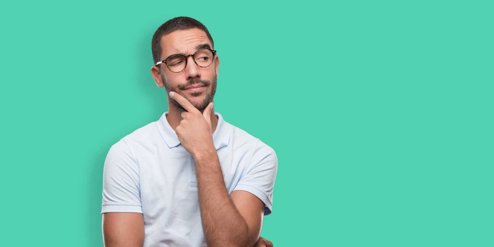 Young man with glasses with hand on chin wondering about genital herpes vs. pimples