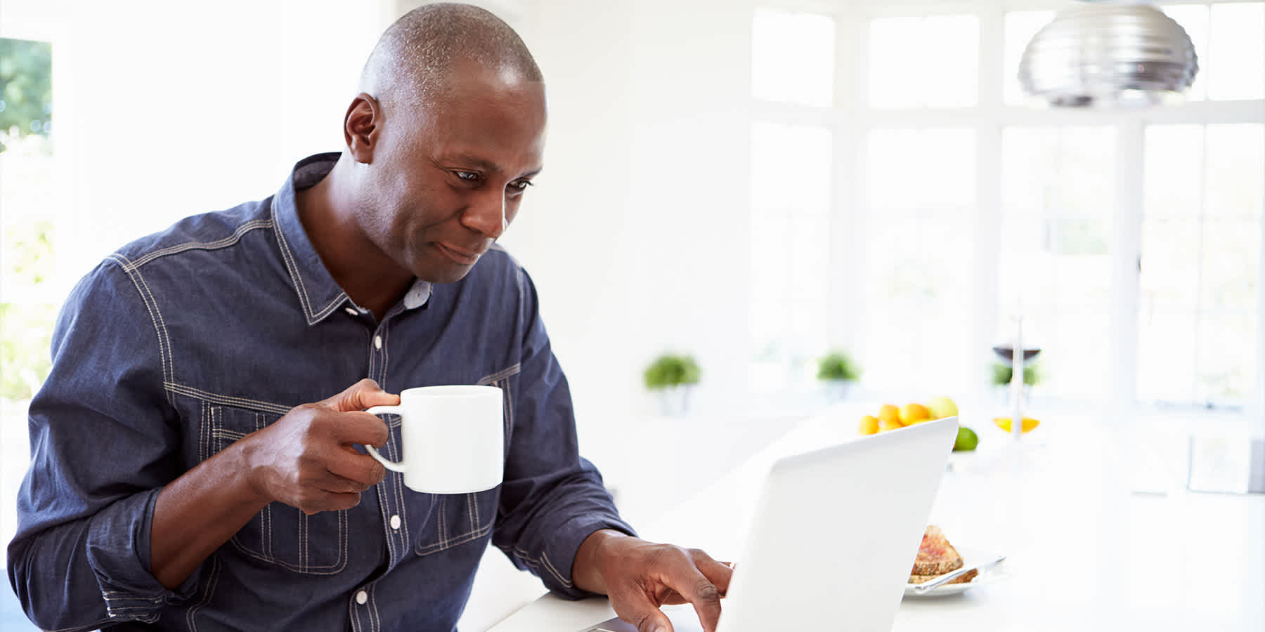 Man holding coffee cup and using laptop to research pearly penile papules vs. HPV