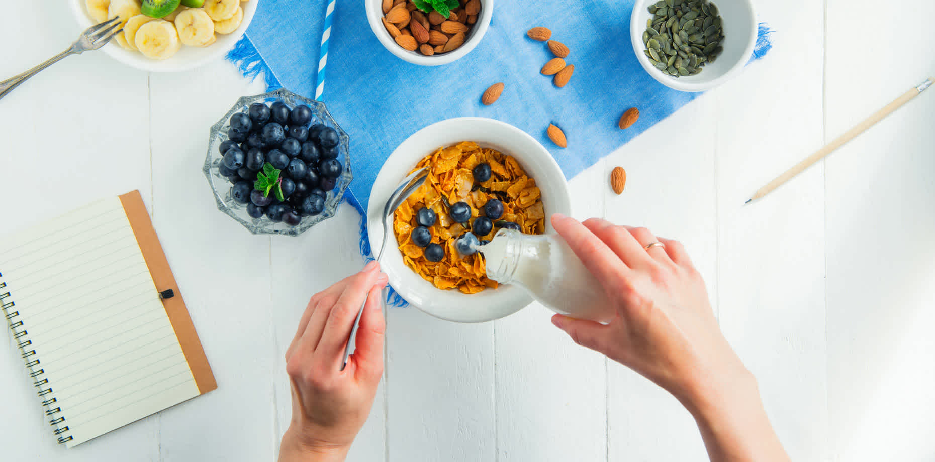 Person pouring bottle of milk on cereal with blueberries