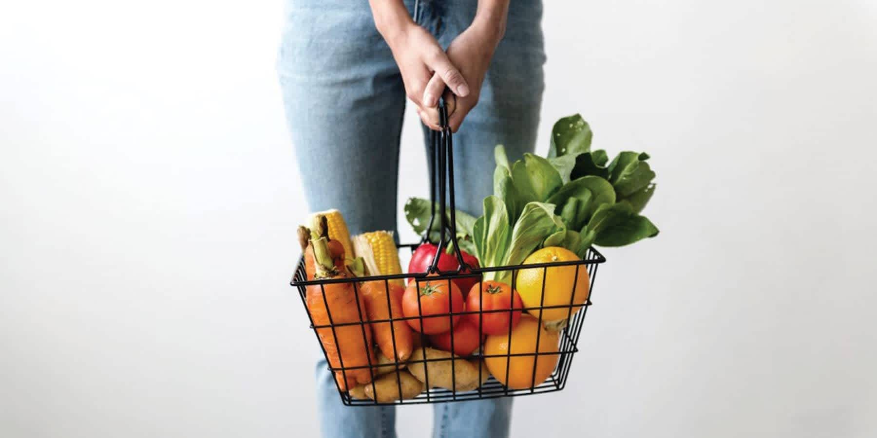 Person holding basket of fruits in front of legs