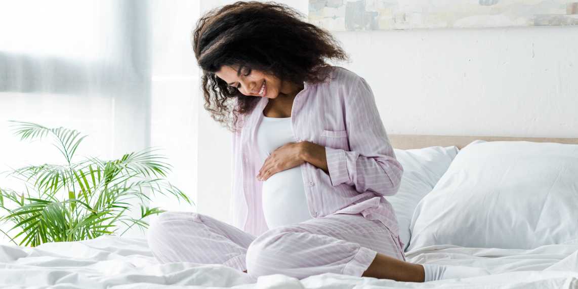 Pregnant woman without type 1 diabetes during pregnancy sitting on bed and smiling