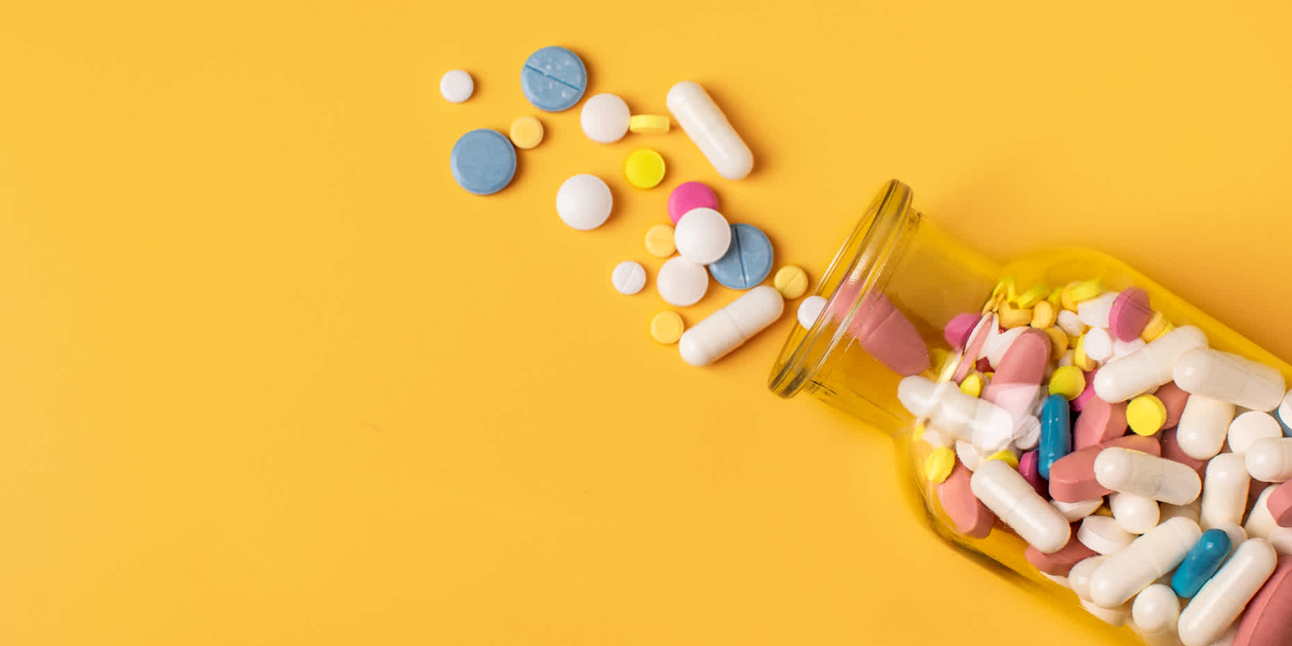 Opened bottle of different vitamins against a yellow background