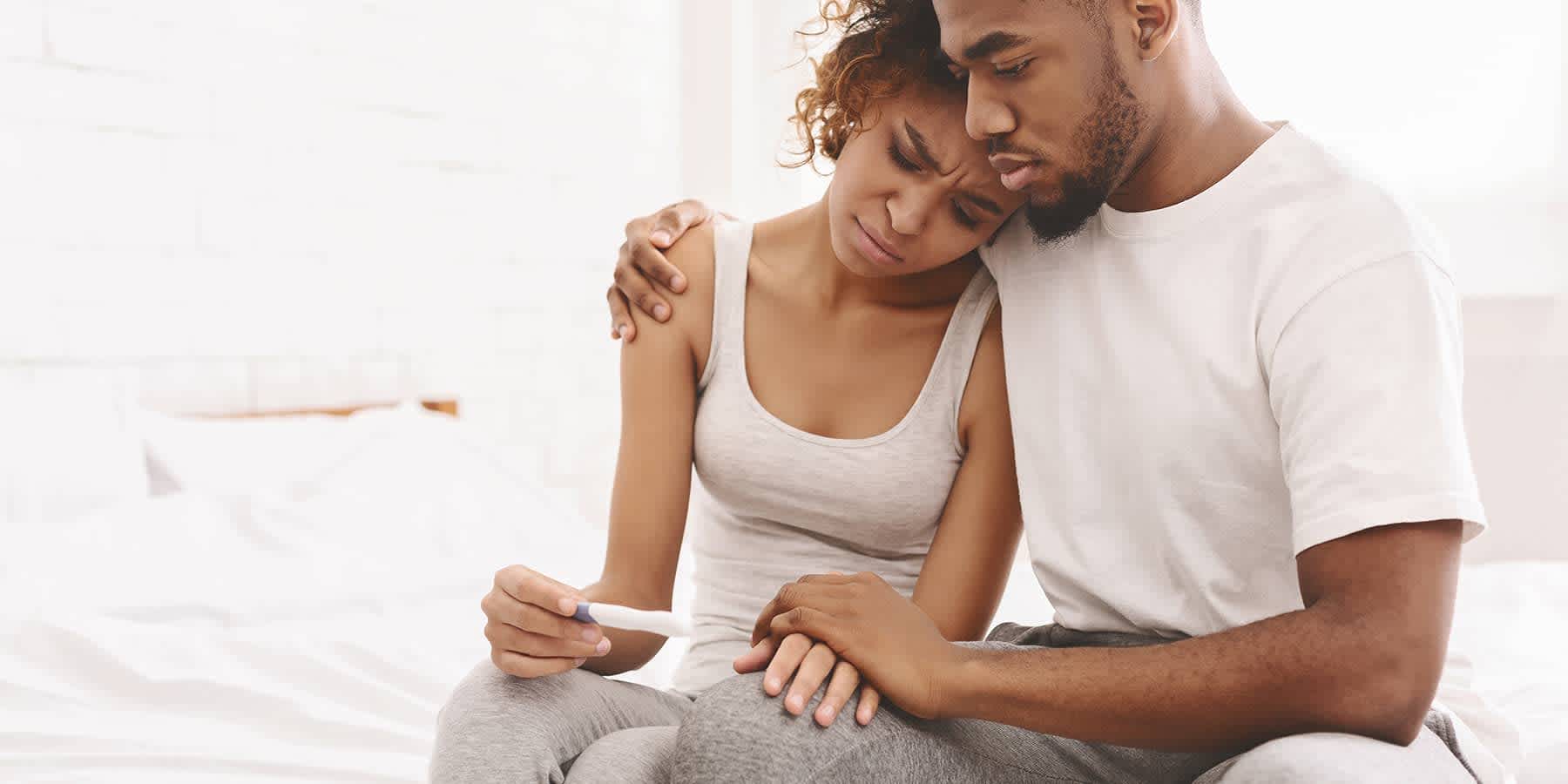 Distraught couple comforting each other while looking at pregnancy test as a sign of infertility in the woman