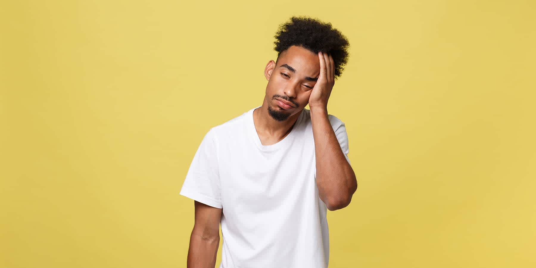 Man standing against yellow background feeling fatigued and wondering about the signs of vitamin D deficiency