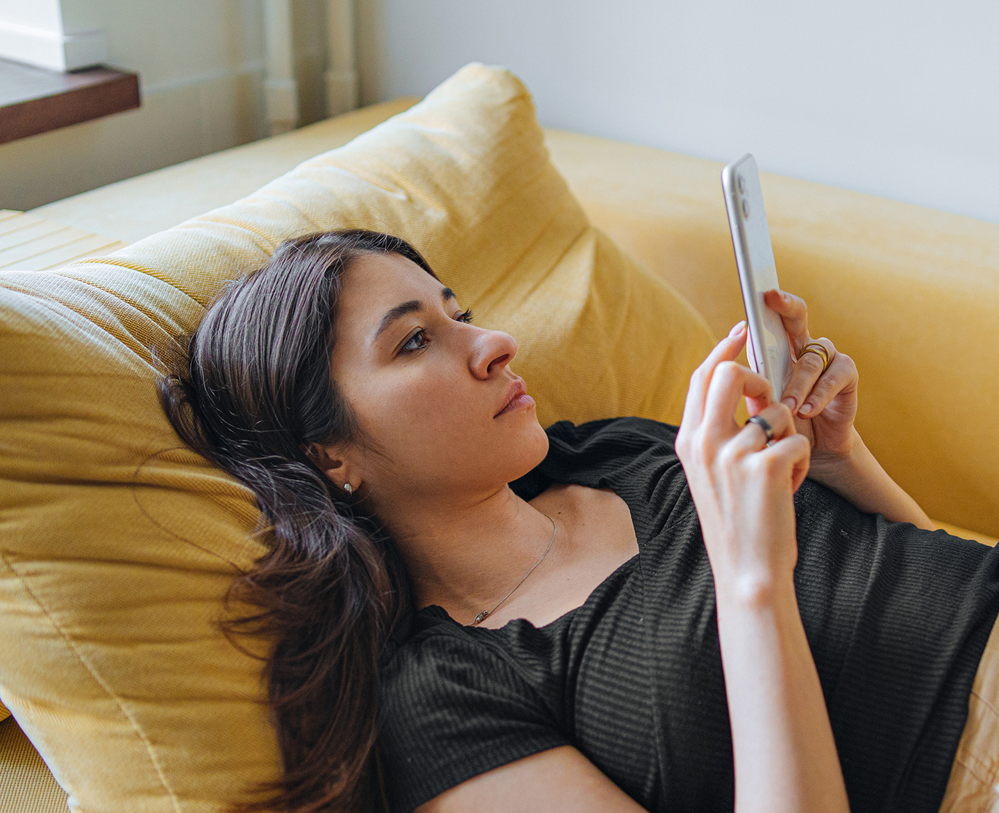 Woman scheduling appointment for UTI treatment online on her mobile phone while lying on couch